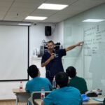 Alasdair pointing at a whiteboard in front of a group of students.